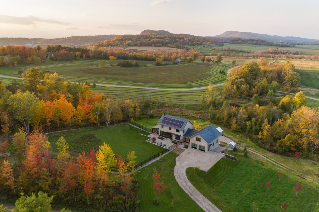 three story net zero farmhouse in the countryside of Vermont, with solar panels on the roof. This is an aerial shot. Luxury house construction example.