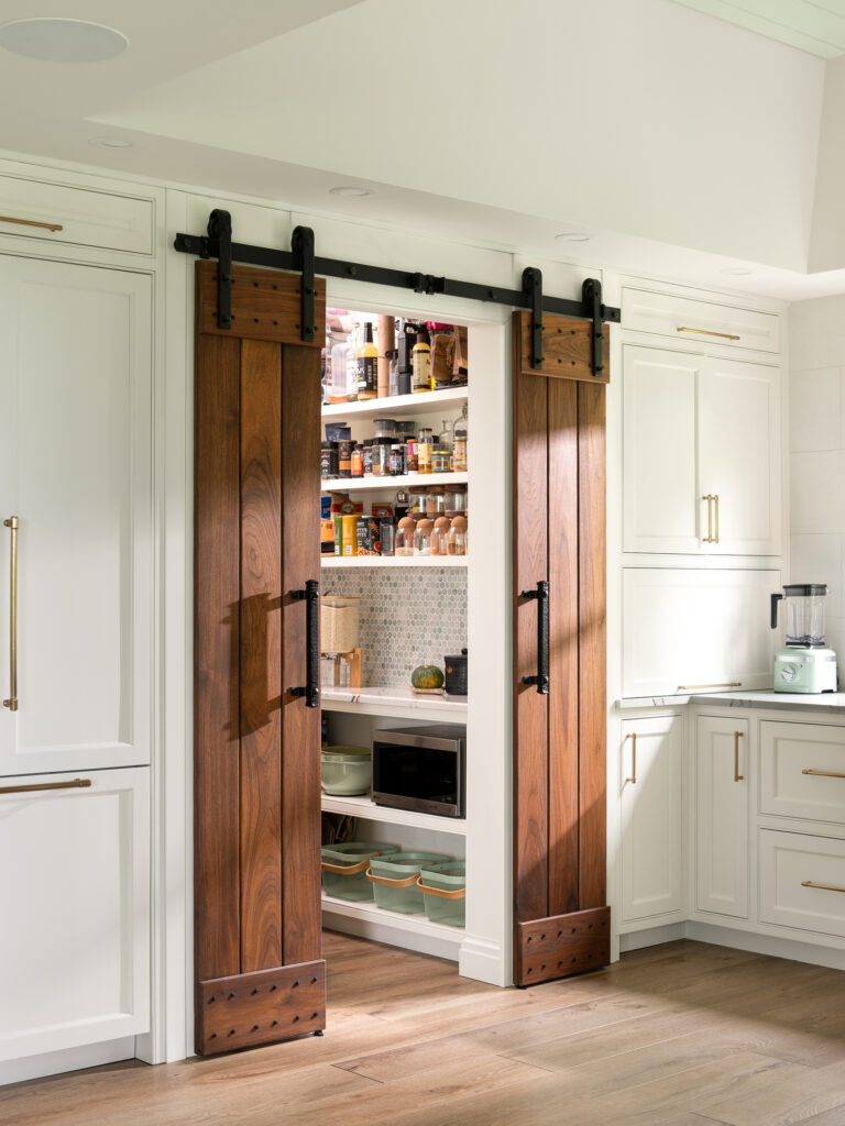 Barn door into a kitchen pantry with white and blue tile and gold accents to show the construction details of a custom home renovation by Silver Maple