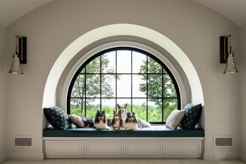 A custom built-in nook underneath an arched window with four small dogs laying down. The window faces a spring day in Vermont.