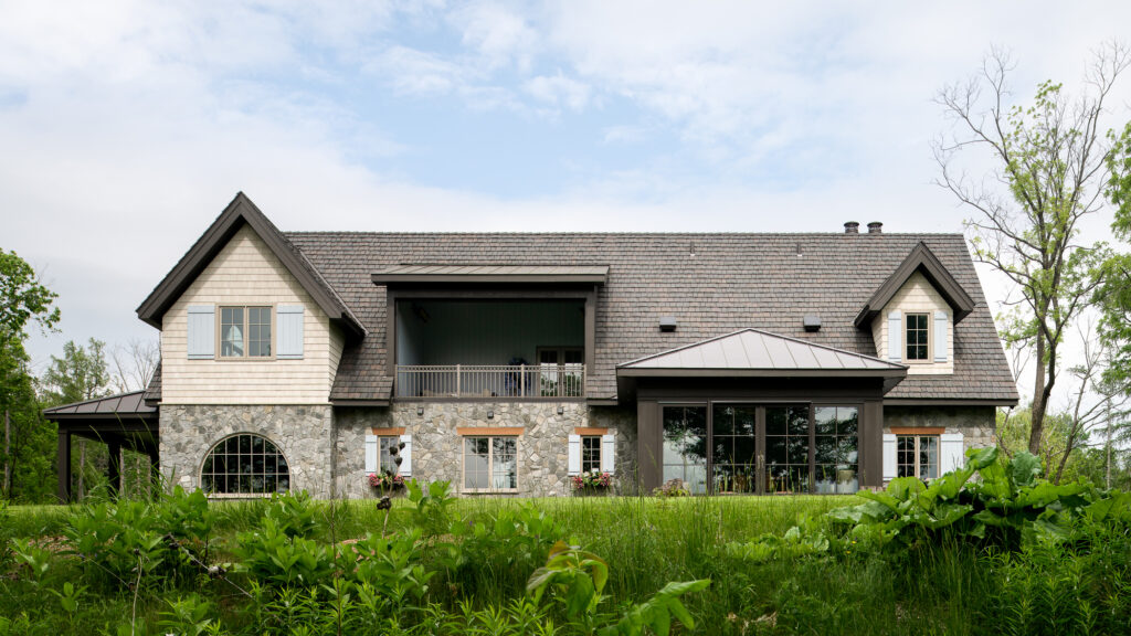 A modern yet whimsical stone house framed by lush green landscape captured before dusk.