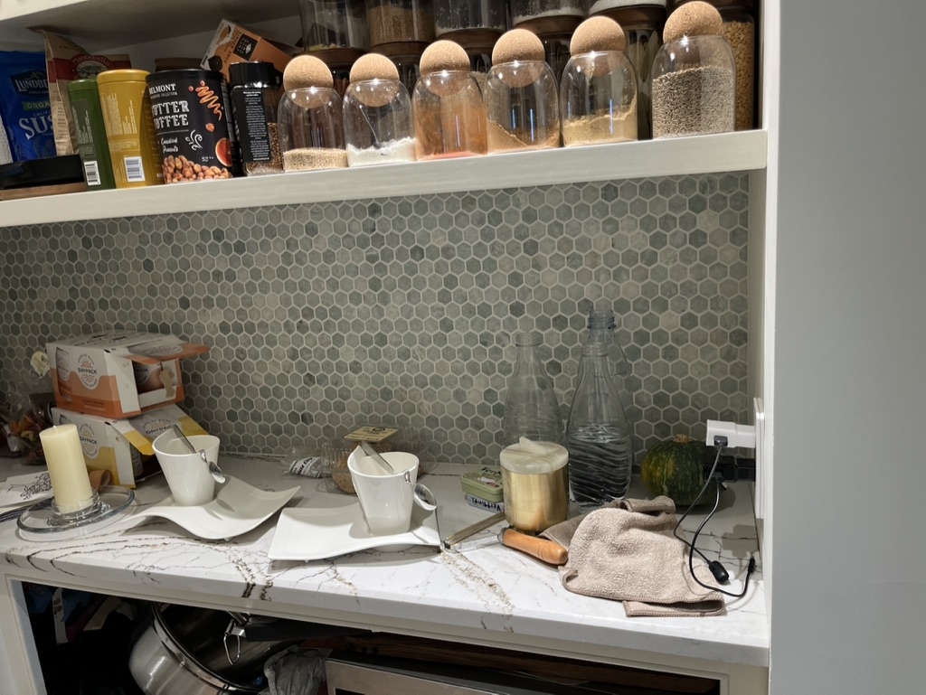 A lived in kitchen pantry with blue and white tile backsplash, coffee mugs, and food storage to reveal the behind the scenes process of a project photoshoot.